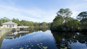 A tranquil lakeside setting with a wooden dock extending into the water, surrounded by lush greenery and a small building with a sloped roof. - Seagrove Highlands by Southern Vacation Rentals (Santa Rosa Beach)