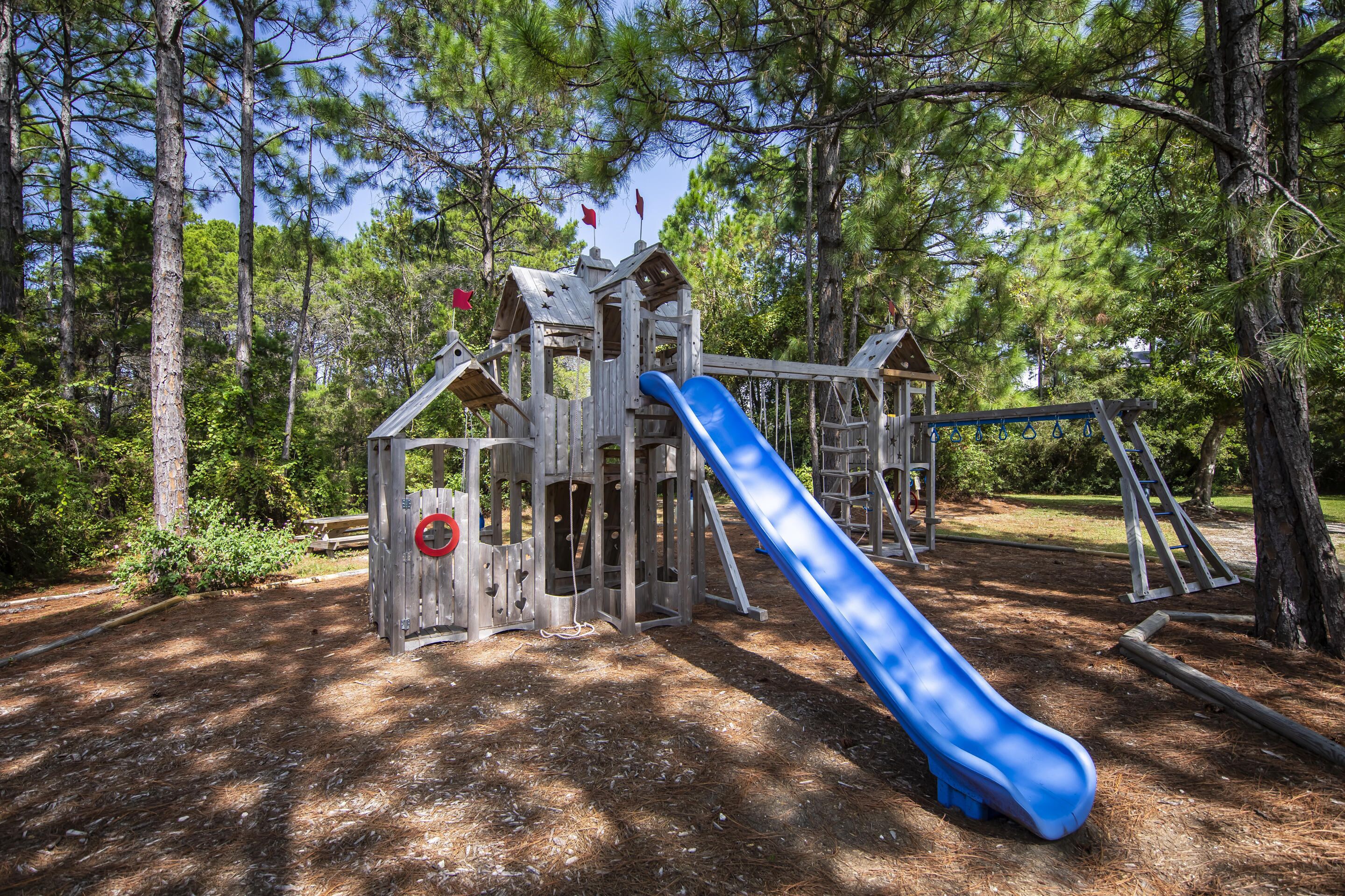 Un'area giochi con uno scivolo blu, strutture in legno per arrampicarsi e una piccola casetta da gioco.