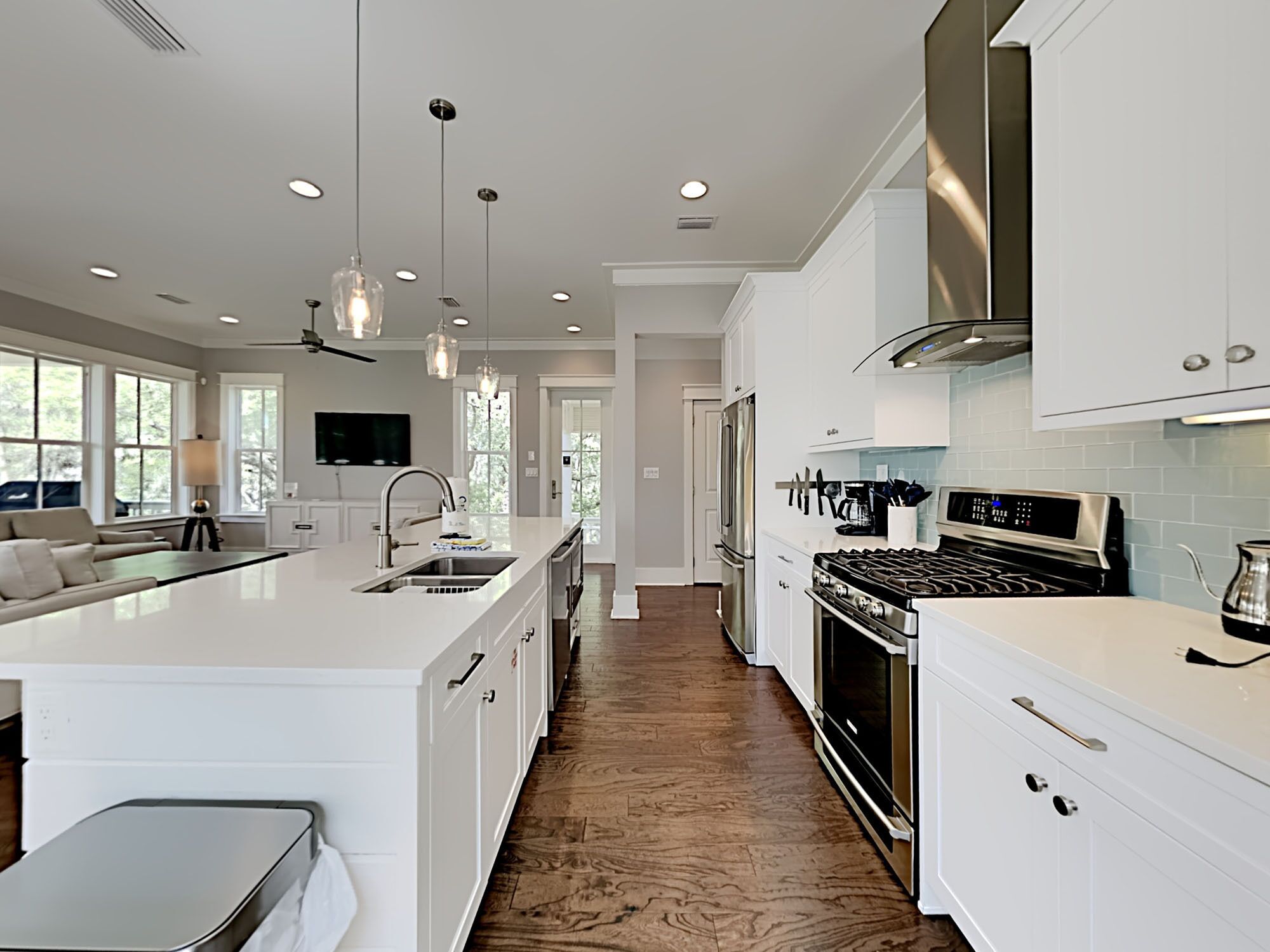 A modern kitchen with white cabinetry, a large island with a sink, stainless steel appliances, pendant lighting, and a view to the outside.