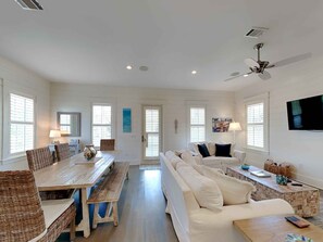 A spacious living area with a wooden dining table, wicker chairs, a white sofa, and a ceiling fan. - Our Treasure by Southern Vacation Rentals (Santa Rosa Beach)