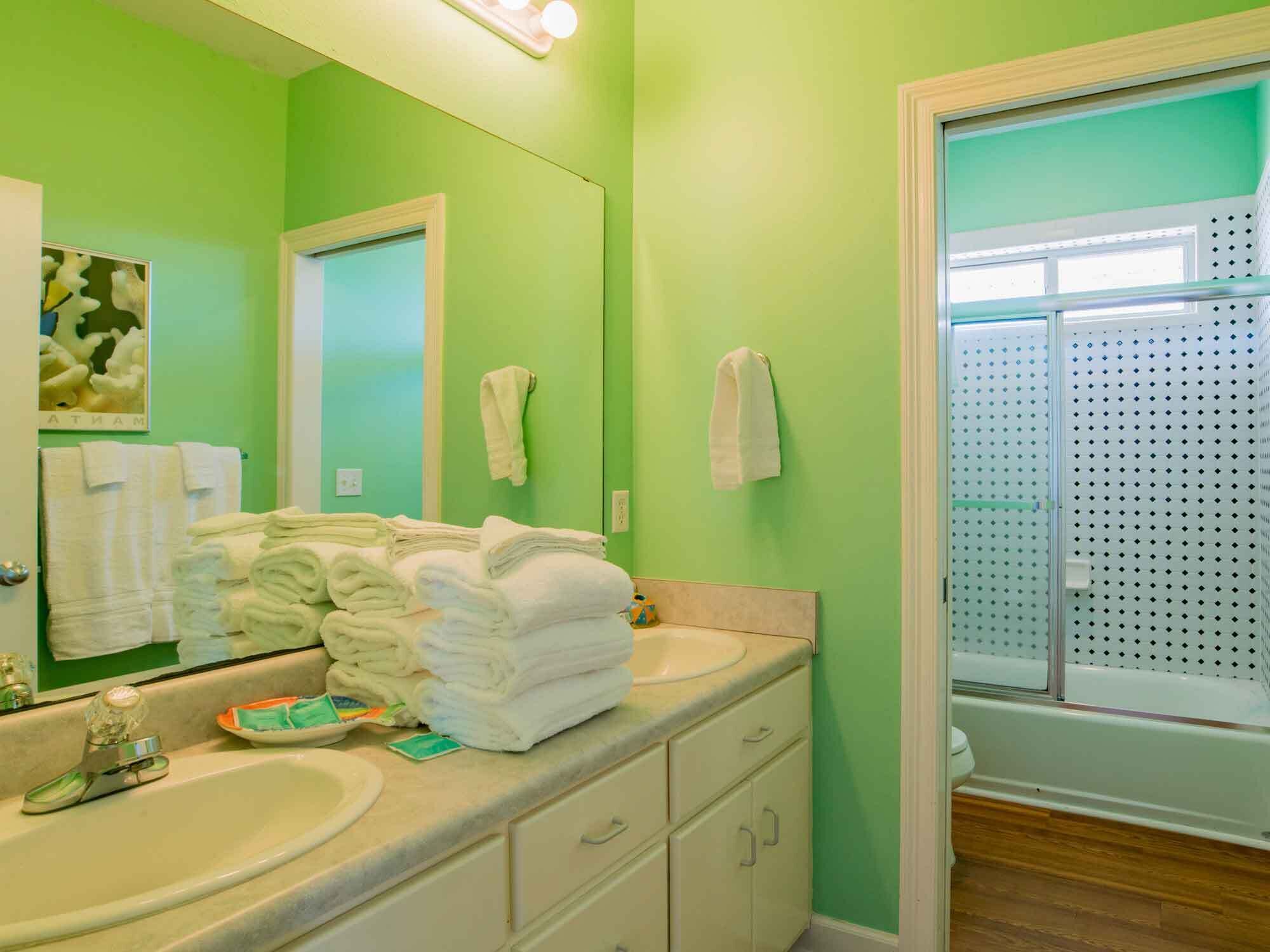 Un baño con paredes verdes, un lavabo, un espejo y una zona de ducha.