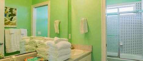 Un baño con paredes verdes, un lavabo, un espejo y una zona de ducha.