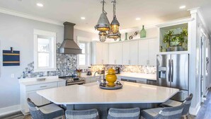 A modern kitchen with a large island, stainless steel appliances, and wicker bar stools. - The Oasis by Resort Collection (Panama City Beach)