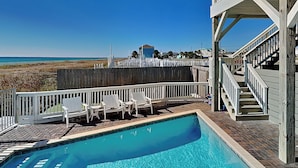 A pool area with a view of the beach, white deck chairs, and a wooden fence. - The Oasis by Resort Collection (Panama City Beach)