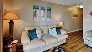 A living room with a beige sofa, two side tables with lamps, and a wooden floor. - Grand Caribbean #210 East by Southern Vacation Rentals (Destin)