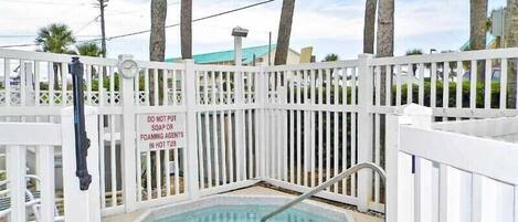 A small outdoor hot tub surrounded by a white fence with a sign prohibiting the use of soap or foaming agents.