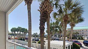 A balcony with a view of a swimming pool, palm trees, and a parking lot with cars. - Grand Caribbean #210 East by Southern Vacation Rentals (Destin)