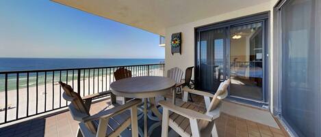 Un balcon avec une table et des chaises, une vue sur la plage et une porte-fenêtre coulissante donnant sur une pièce intérieure.