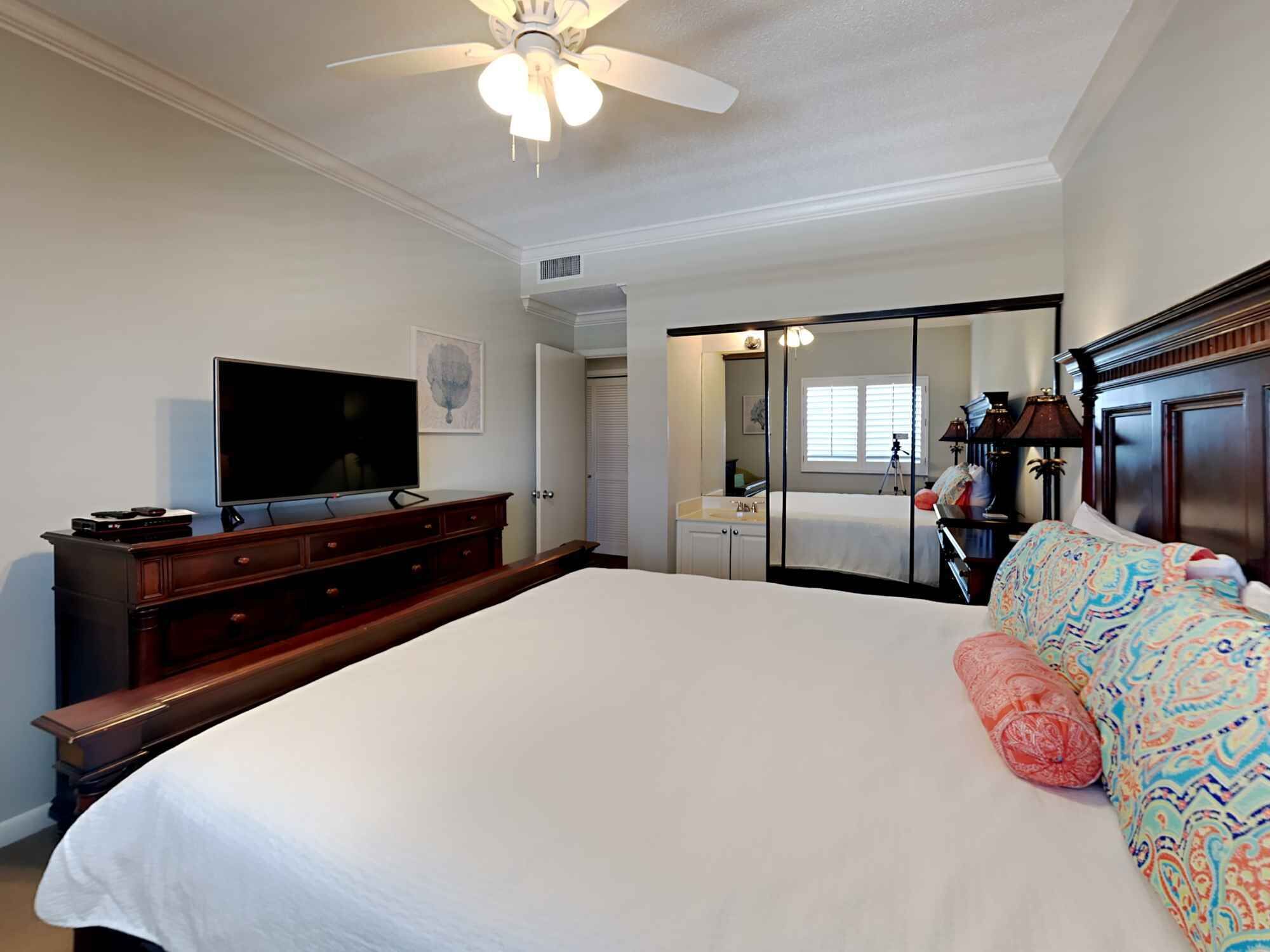 A bedroom with a large bed, a television, a dresser, a mirror, and a wardrobe.