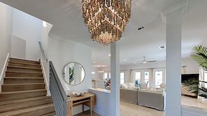 A modern interior with a wooden staircase, a round mirror, a chandelier, and a living area with a sofa and chairs. - Juela on the Beach by Southern Vacation Rentals (Pensacola Beach)