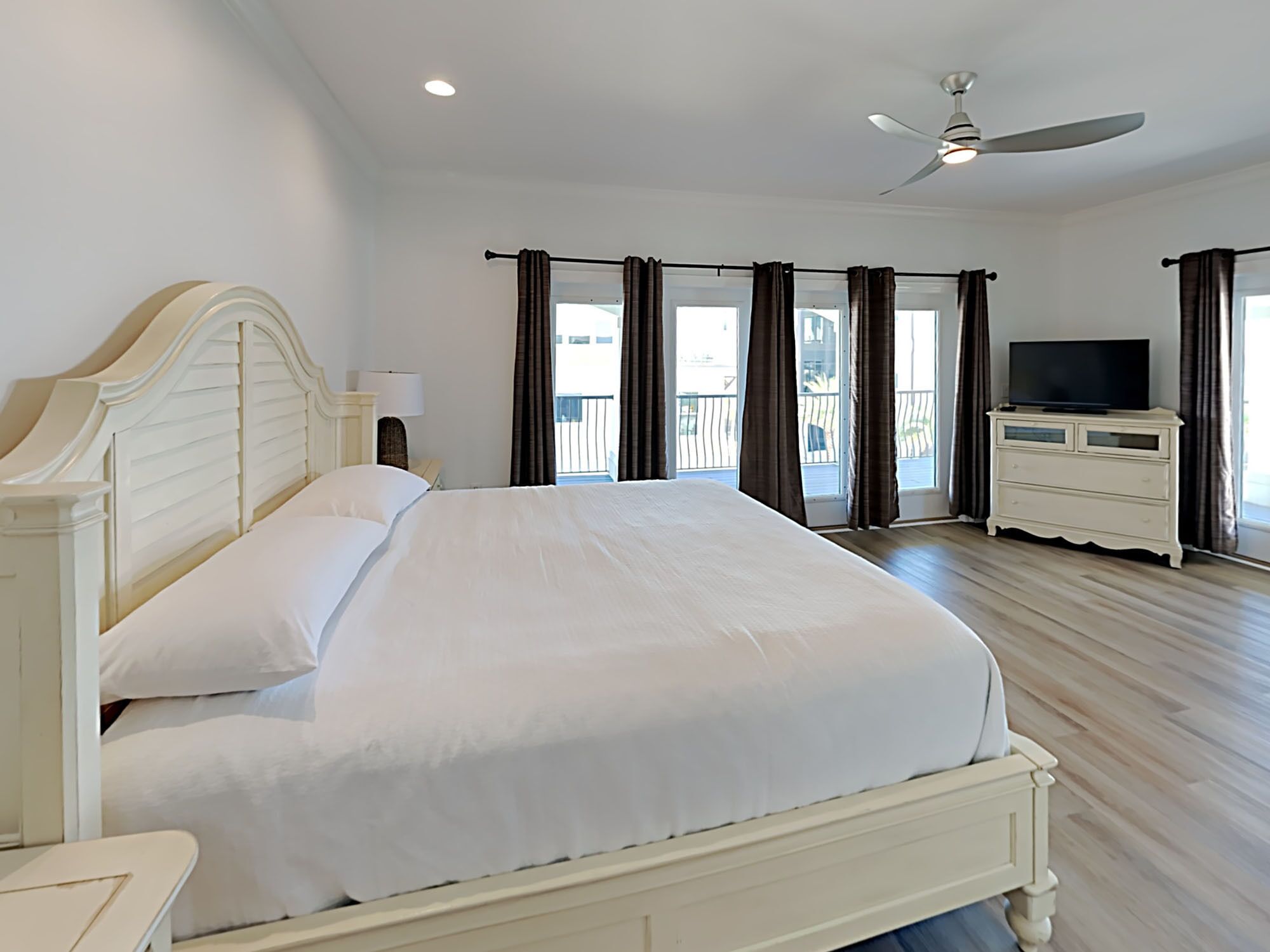 A hotel room with a large bed, a television on a dresser, and a balcony with curtains.