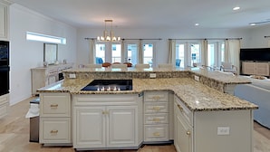 A spacious kitchen with granite countertops, white cabinetry, and a central island. - Juela on the Beach by Southern Vacation Rentals (Pensacola Beach)
