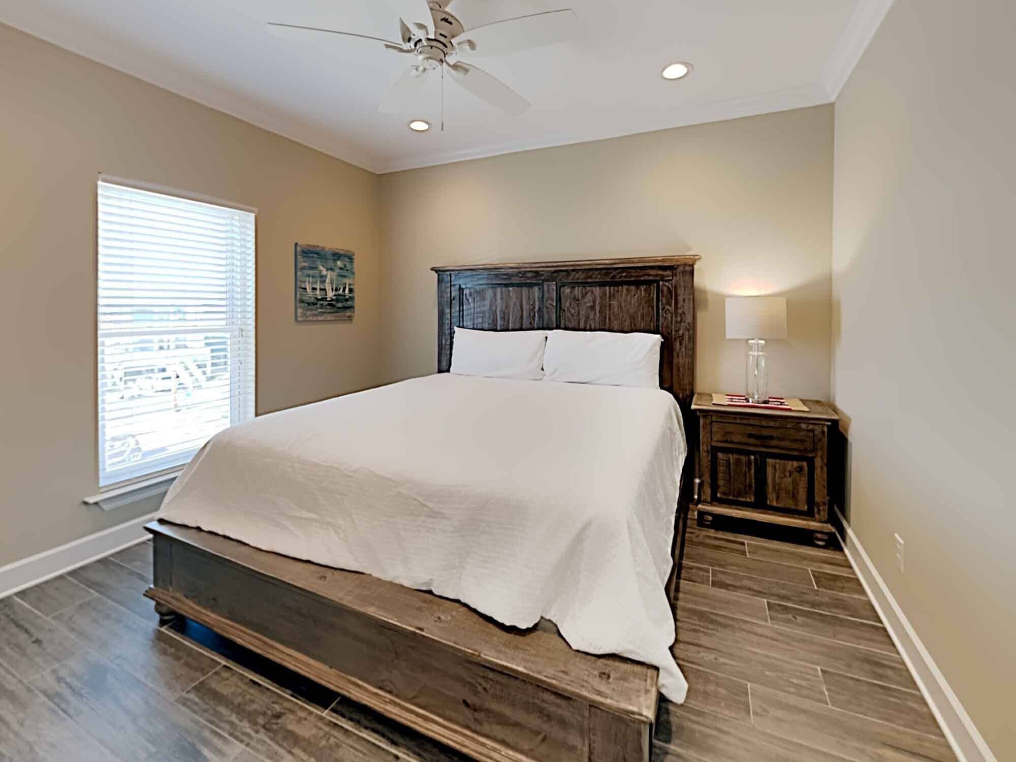 Une chambre à coucher avec un lit en bois, un ventilateur de plafond, une table de chevet avec une lampe et une fenêtre avec des stores.