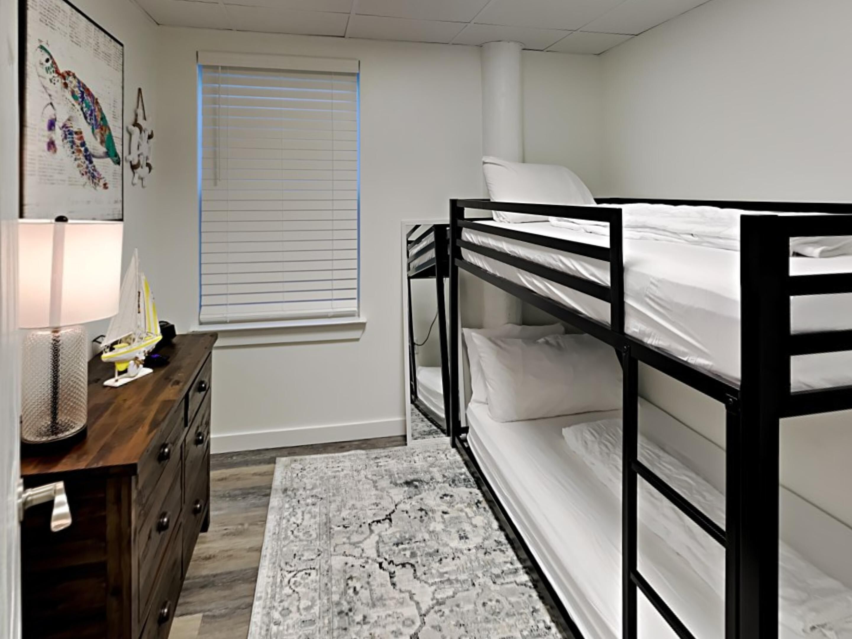 A bunk bed room with a desk, a lamp, and a window with blinds.