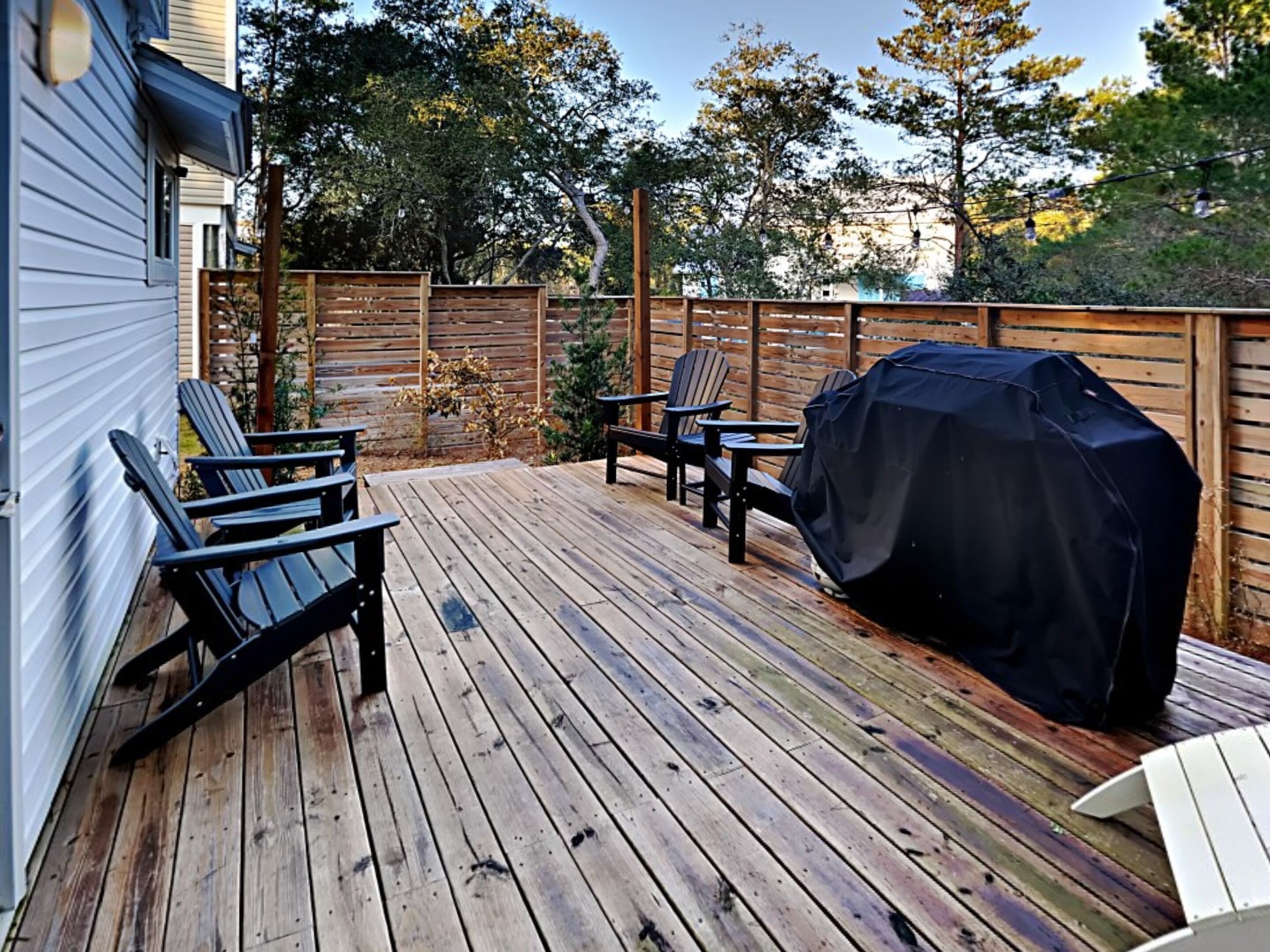 En træterrasse med Adirondack-stole og grill.