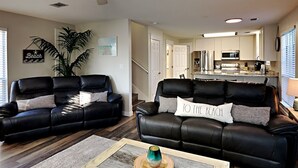 A living room with two black leather sofas, a coffee table, and a staircase leading to a kitchen. - Dune Our Thing by Southern Vacation Rentals (Santa Rosa Beach)