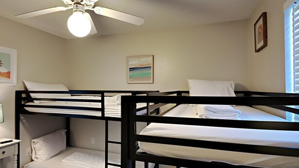 A bunk bed room with a ceiling fan, a painting on the wall, and a window with blinds.