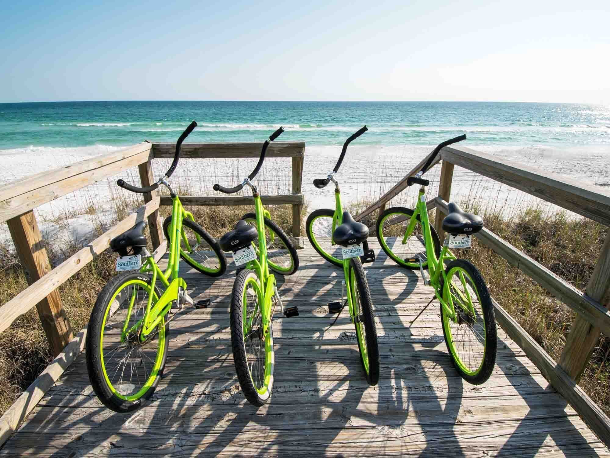 Three bicycles parked on a wooden boardwalk by the beach.