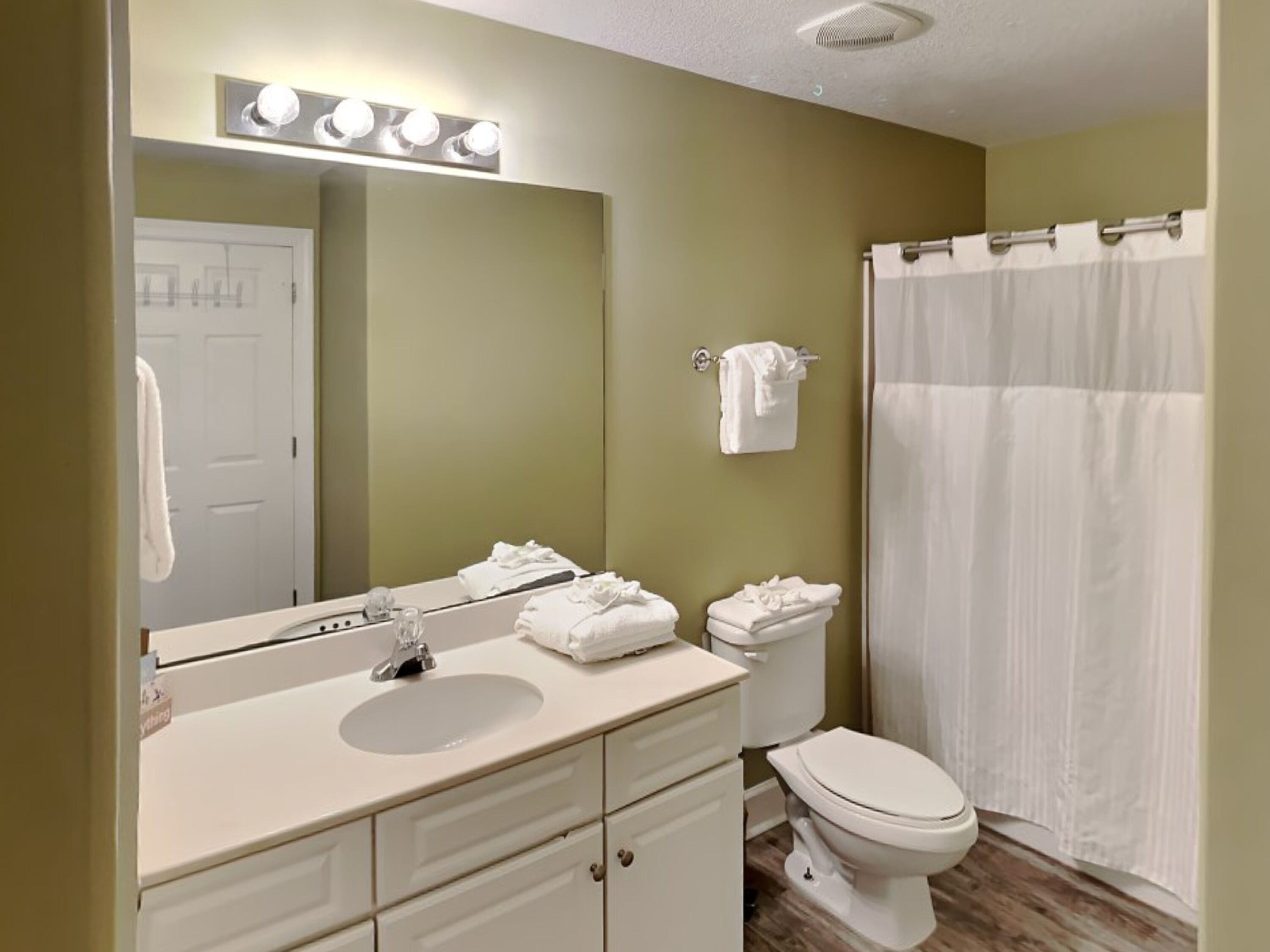 A bathroom with a sink, mirror, and toilet. There are towels hanging on the wall and a shower curtain.