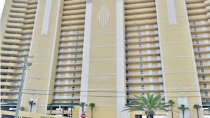 A multi-story hotel with a yellow facade, balconies on each floor, and a prominent emblem in the center. - Emerald Isle by Resort Collection (Panama City Beach)