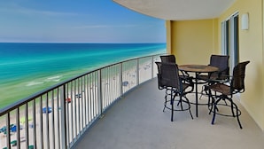 A balcony with a view of the ocean, a table with chairs, and a yellow wall. - Emerald Isle by Resort Collection (Panama City Beach)