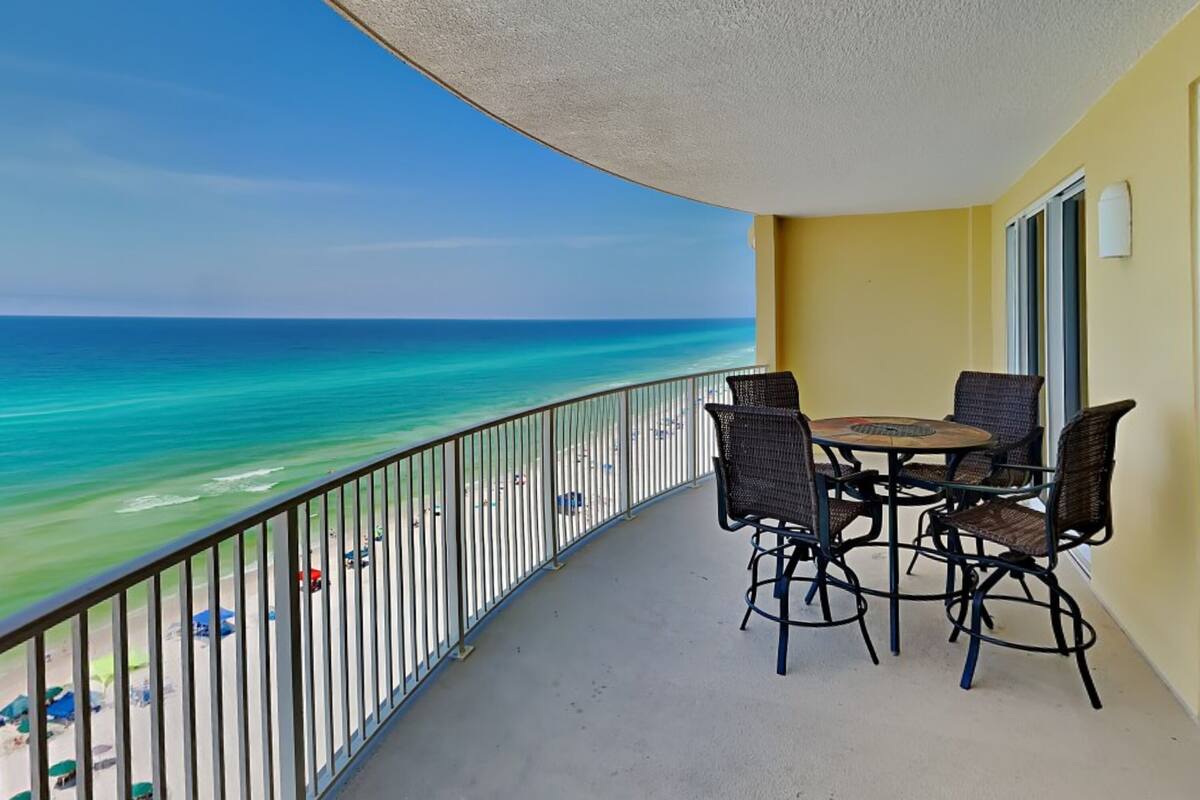 A balcony with a view of the ocean, a table with chairs, and a yellow wall.