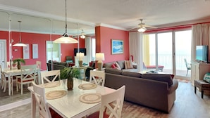 A spacious living area with a dining table, chairs, a sofa, and a balcony with a view. - Emerald Isle by Resort Collection (Panama City Beach)