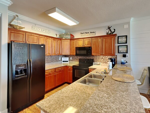 A kitchen with wooden cabinets, a black refrigerator, a microwave, and granite countertops.