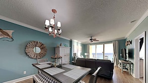 A dining area with a table set for four, a chandelier, and a view of the ocean through large windows. - Emerald Isle by Resort Collection (Panama City Beach)