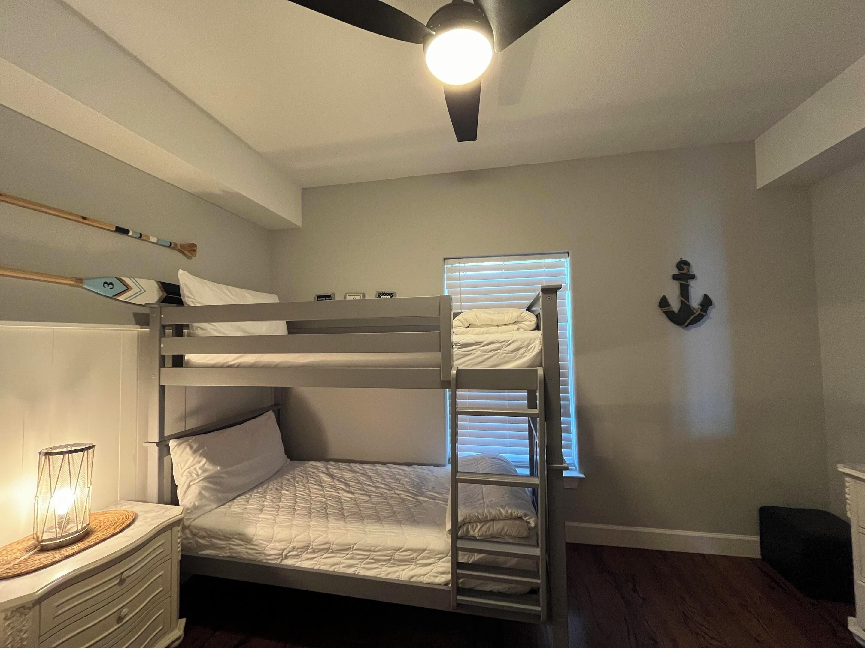 A bunk bed room with a ceiling fan, a small table with a lantern, and a wall-mounted anchor decoration.