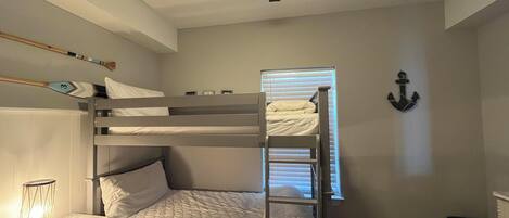 A bunk bed room with a ceiling fan, a small table with a lantern, and a wall-mounted anchor decoration.