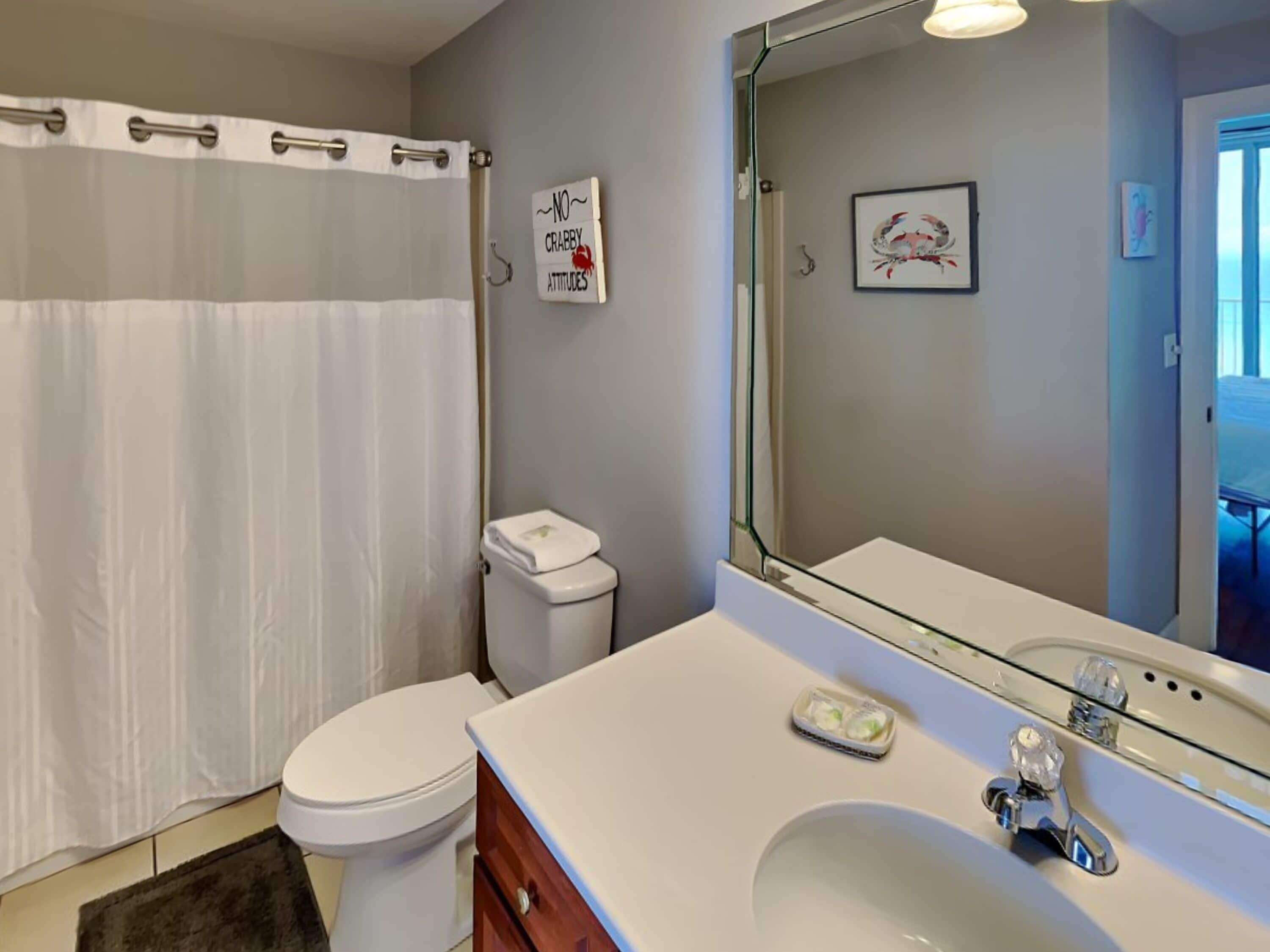 A bathroom with a white toilet, a sink with a mirror, and a shower curtain.