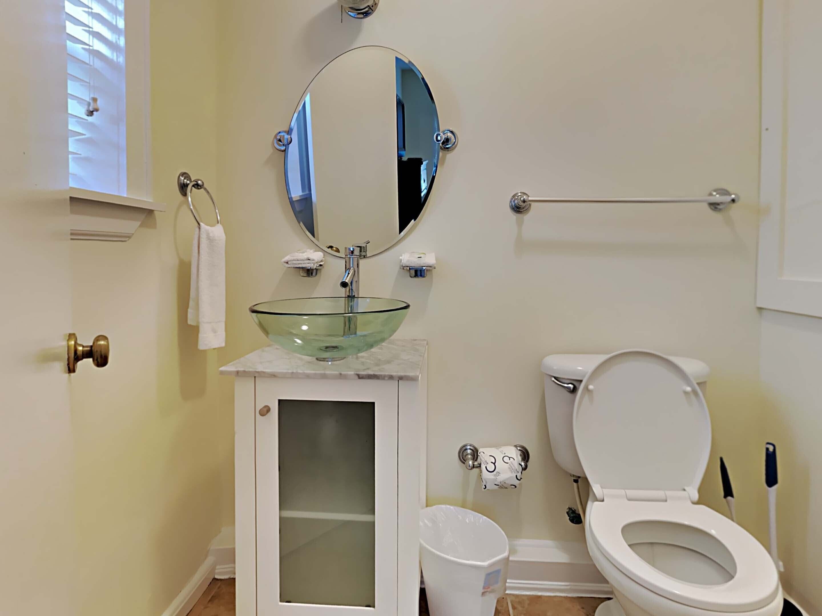 A bathroom with a glass sink, a toilet, a mirror, and a towel rack.