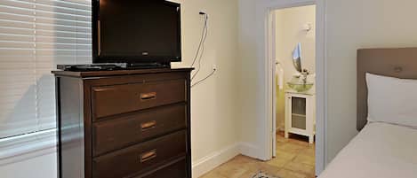 Een slaapkamer met een televisie op een dressoir, een bed, een badkamer met een wastafel en spiegel, en een deur die leidt naar een andere kamer.