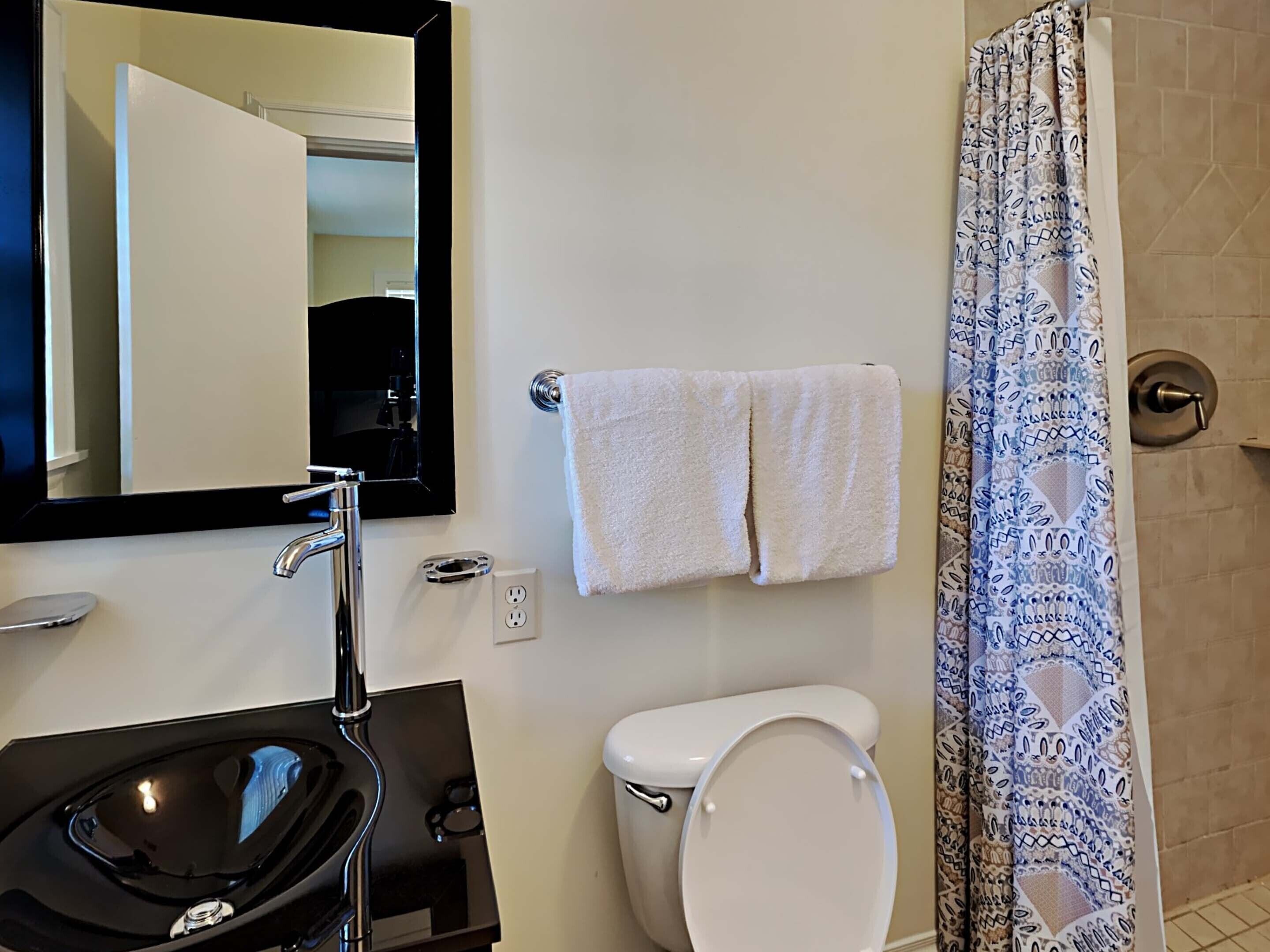 A bathroom with a sink, mirror, toilet, and shower curtain.