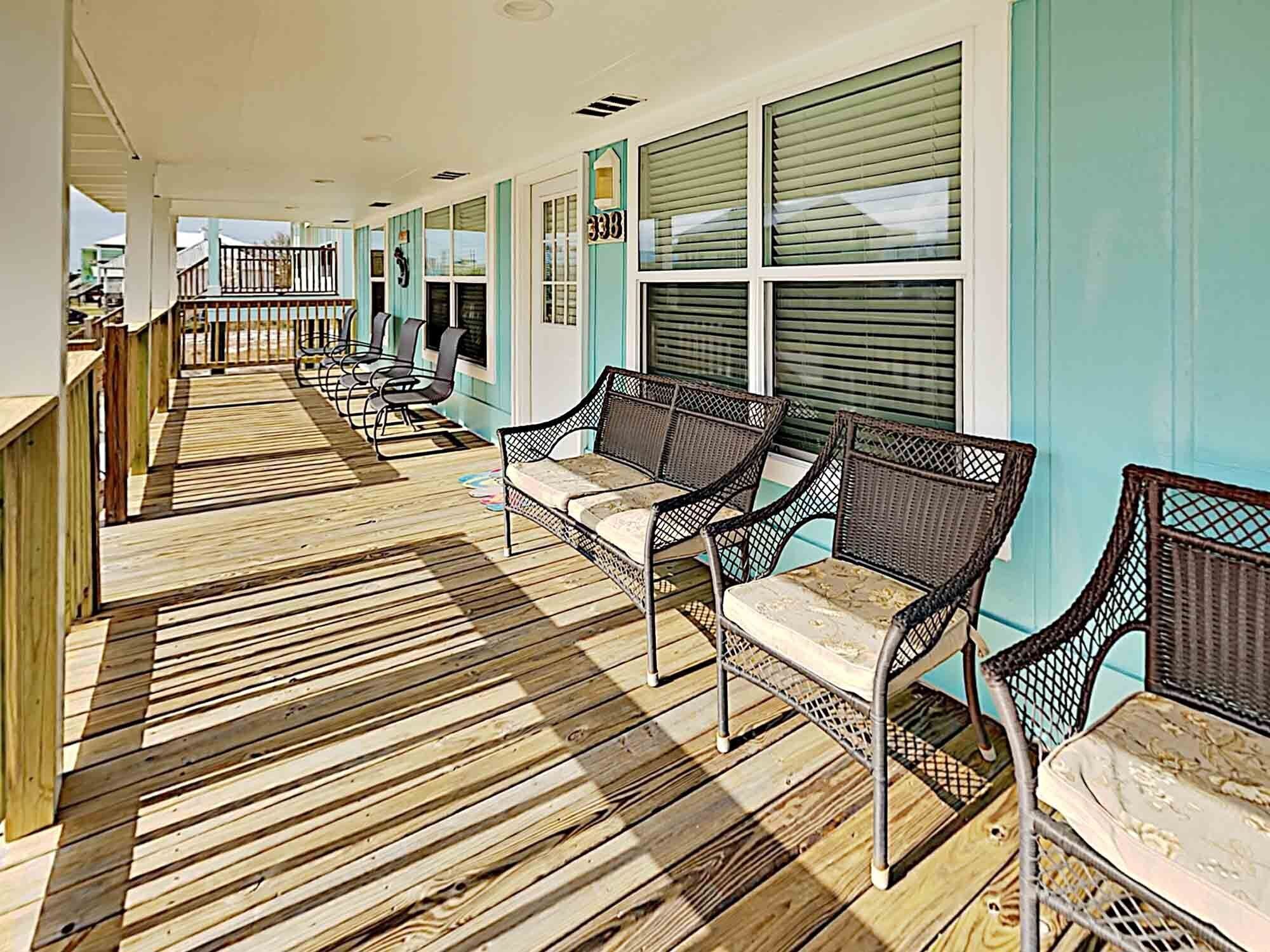 A covered outdoor area with wooden flooring, wicker furniture, and a view of the ocean.