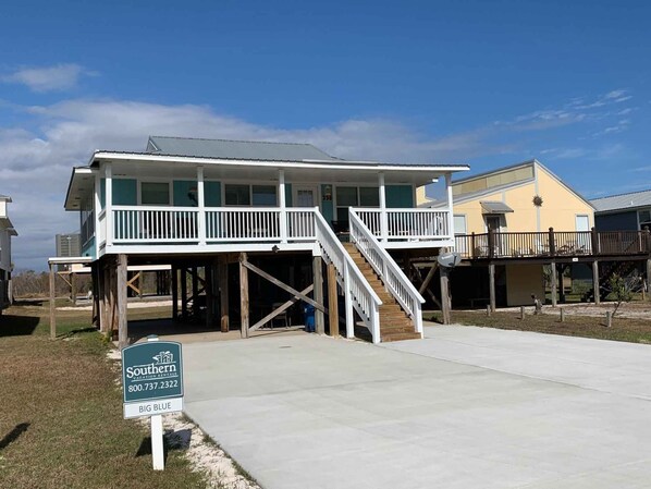 A two-story beachfront property with a balcony, a staircase, and a sign for Southern Vacation Rentals.
