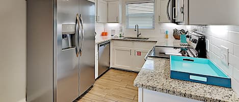 A modern kitchen with stainless steel appliances, white cabinetry, and a granite countertop.