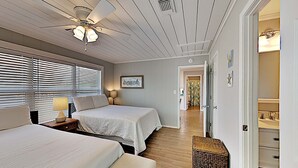 A bedroom with two beds, a ceiling fan, a window with blinds, a bedside lamp, and a wicker basket. - Big Blue by Southern Vacation Rentals (Gulf Shores)