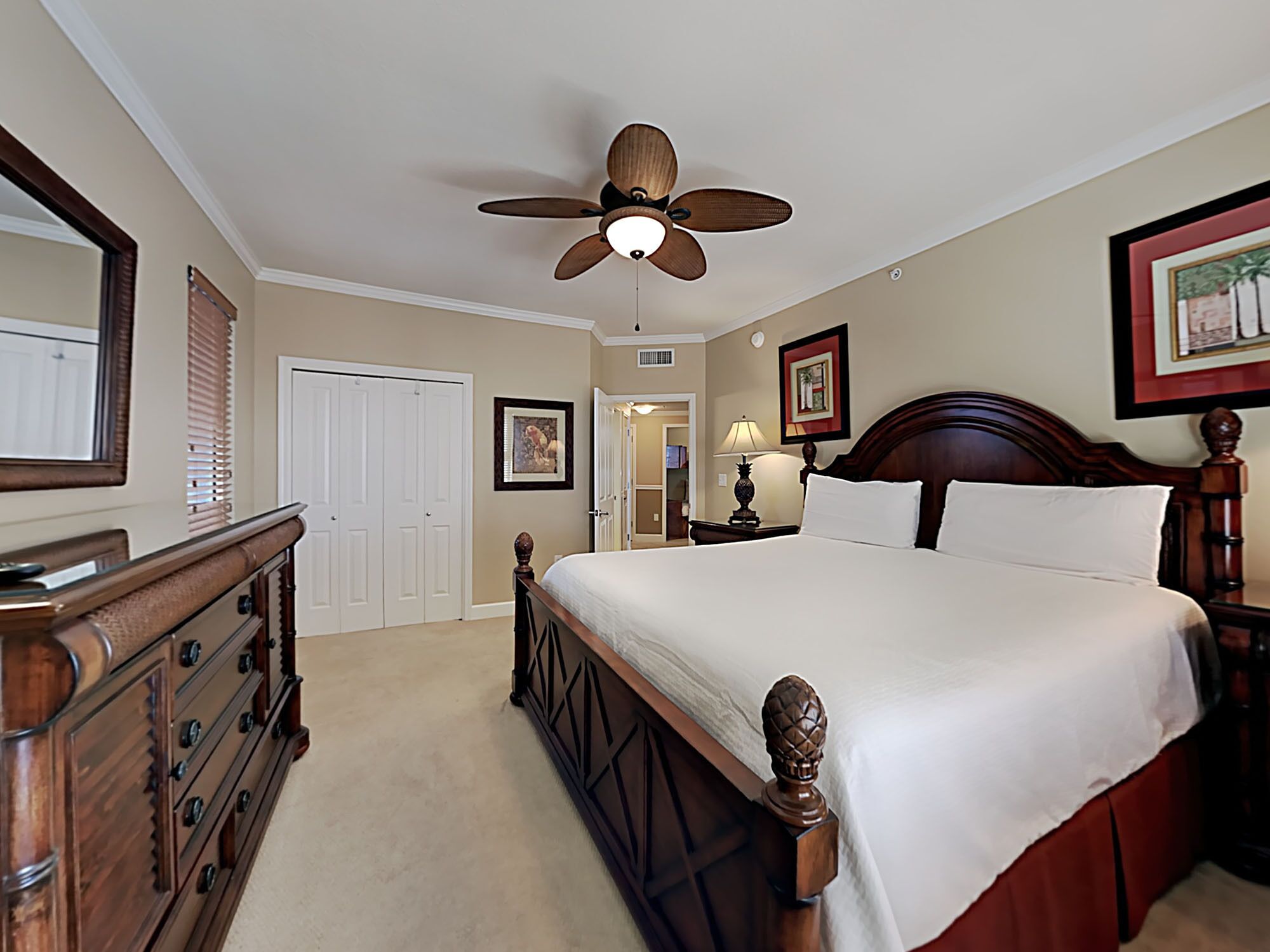 A bedroom with a wooden bed, a ceiling fan, a dresser, and a door.