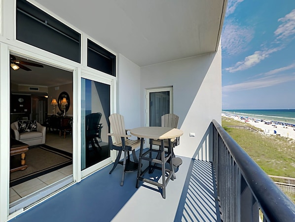 A balcony with a table and chairs, a view of the beach, and a glimpse of the interior.
