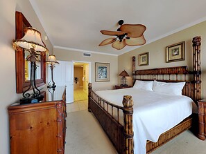 Een ruime slaapkamer met een groot bed, houten hoofdeinde en een plafondventilator.