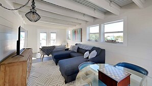 A spacious living room with a sofa, a glass table with a chessboard, and a television on a wooden cabinet. - View From The Top by Southern Vacation Rentals (Santa Rosa Beach)