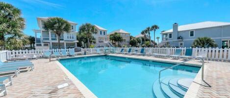 A swimming pool with lounge chairs and a white picket fence.