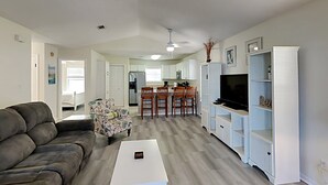 Ein modernes Wohnzimmer mit einem grauen Sofa, einem weißen Couchtisch und einem Essbereich mit Holzstühlen und einem weißen Schrank.
