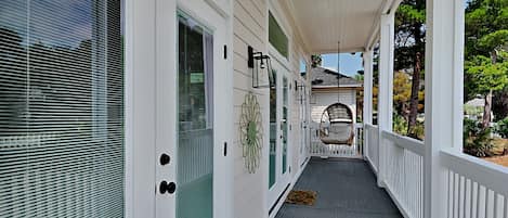A covered porch with a swing chair, white railings, and a view of the garden.