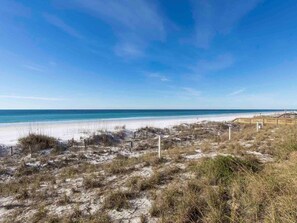 A beach with a wooden boardwalk leading to the ocean, sandy dunes, and sparse vegetation.