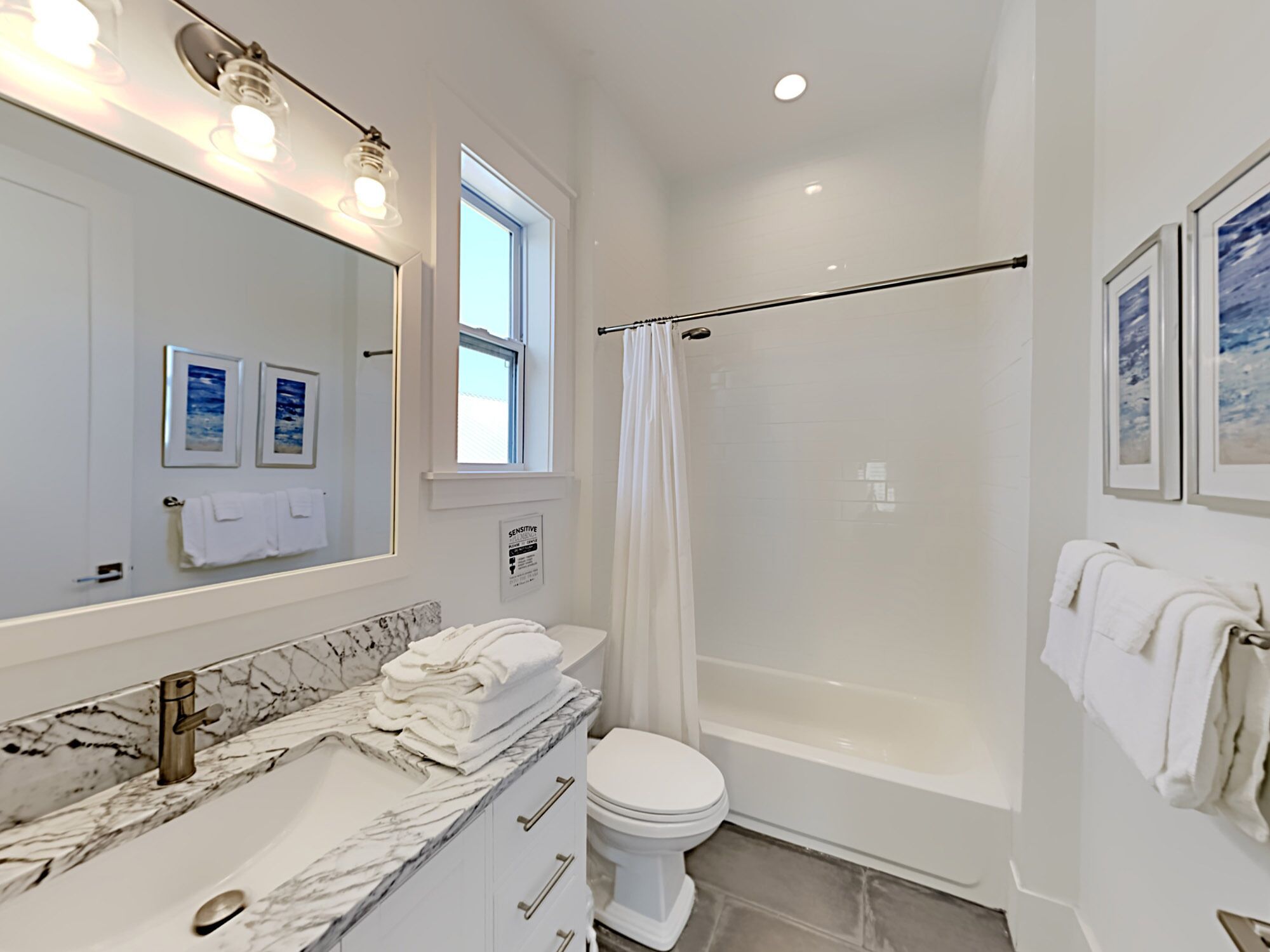 A bathroom with a marble sink, a toilet, a bathtub, and a shower curtain. There are towels on the sink and a window above the shower.