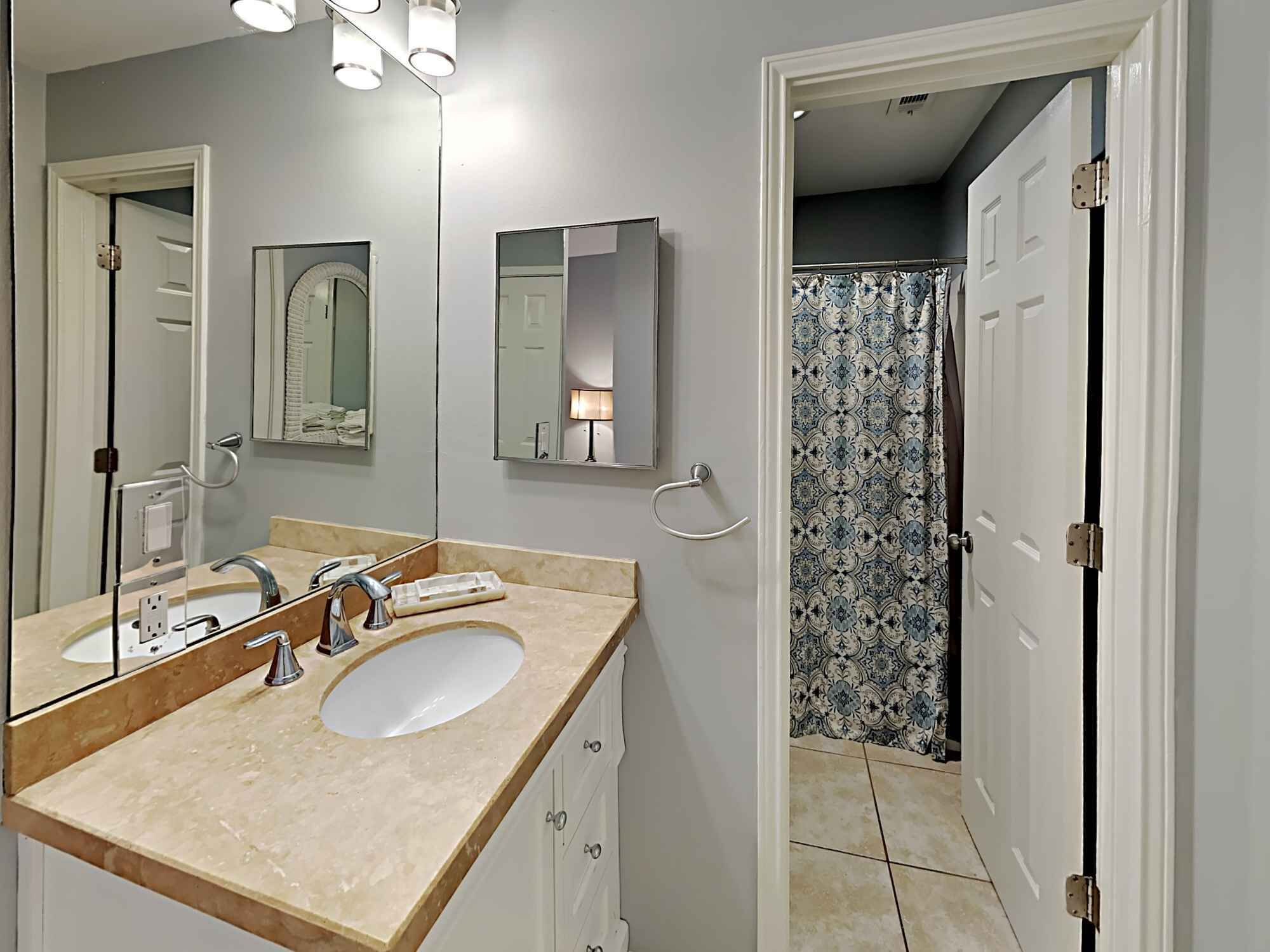 Une salle de bain avec un double lavabo, un miroir, un porte-serviettes et une douche avec des rideaux à motifs.