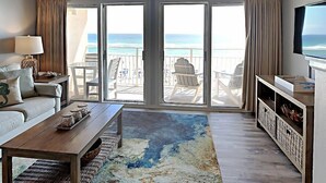 A beach house interior with a sofa, coffee table, TV, and a view of the ocean through large sliding doors. - Crystal Sands #311A by Southern Vacation Rentals (Destin)